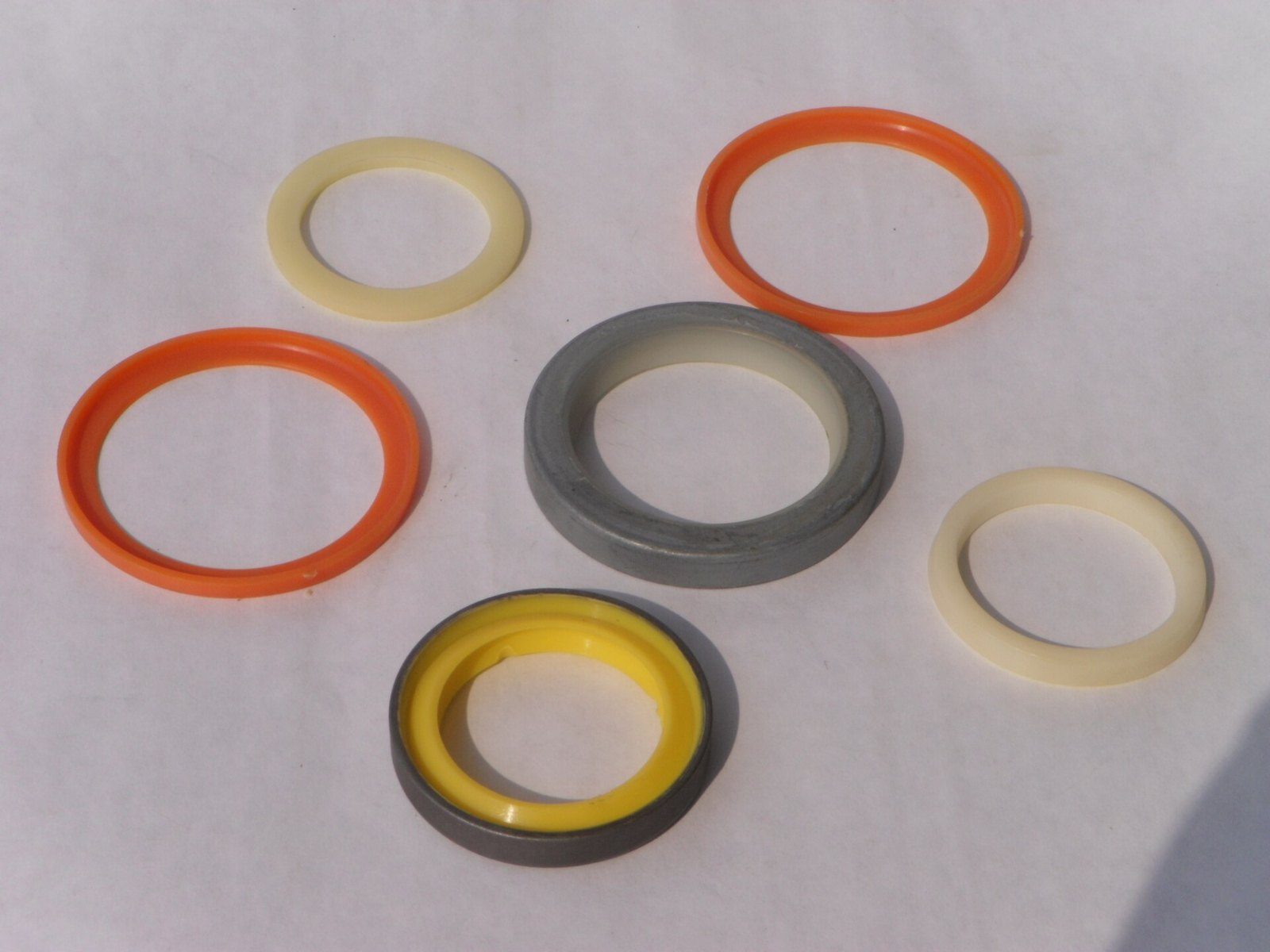 Seis anillos de sellado de distintos tamaños y colores (naranja, amarillo con aro metálico, crema y gris) sobre una superficie clara