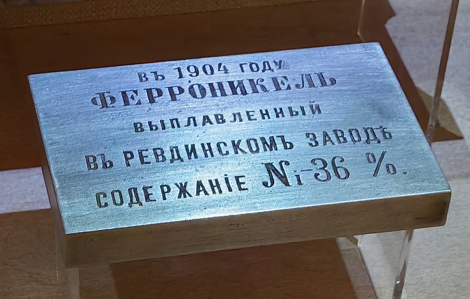 Lingote plateado de ferroníquel expuesto en una vitrina de museo, con una placa en ruso