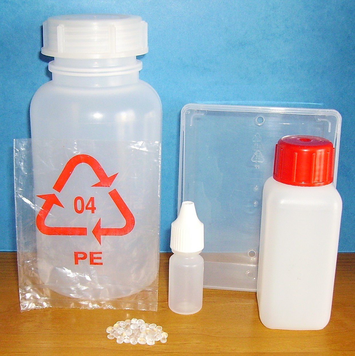 Translucent plastic bottle, jar, box and dropper bottle next to a few pellets, with the recycling symbol 04 PE printed on a bag
