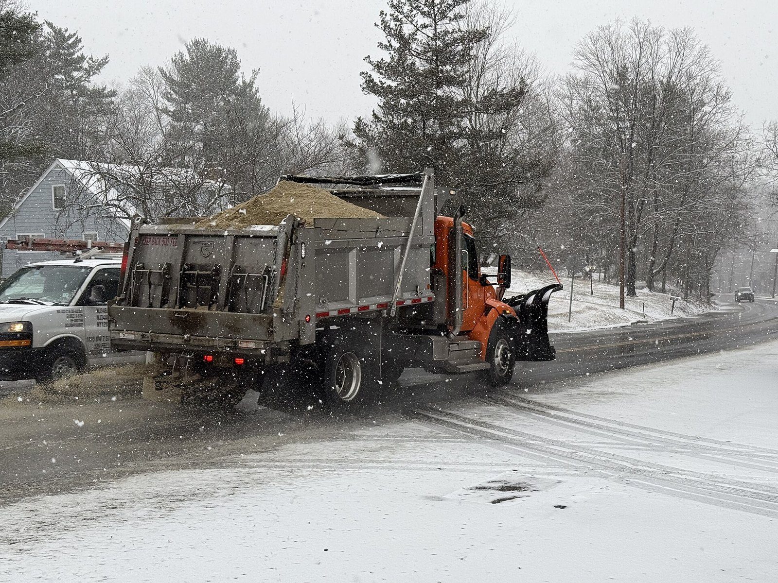 Public works dump truck with a bed loaded with salt and sand driving along a road in light snowfall in New Jersey