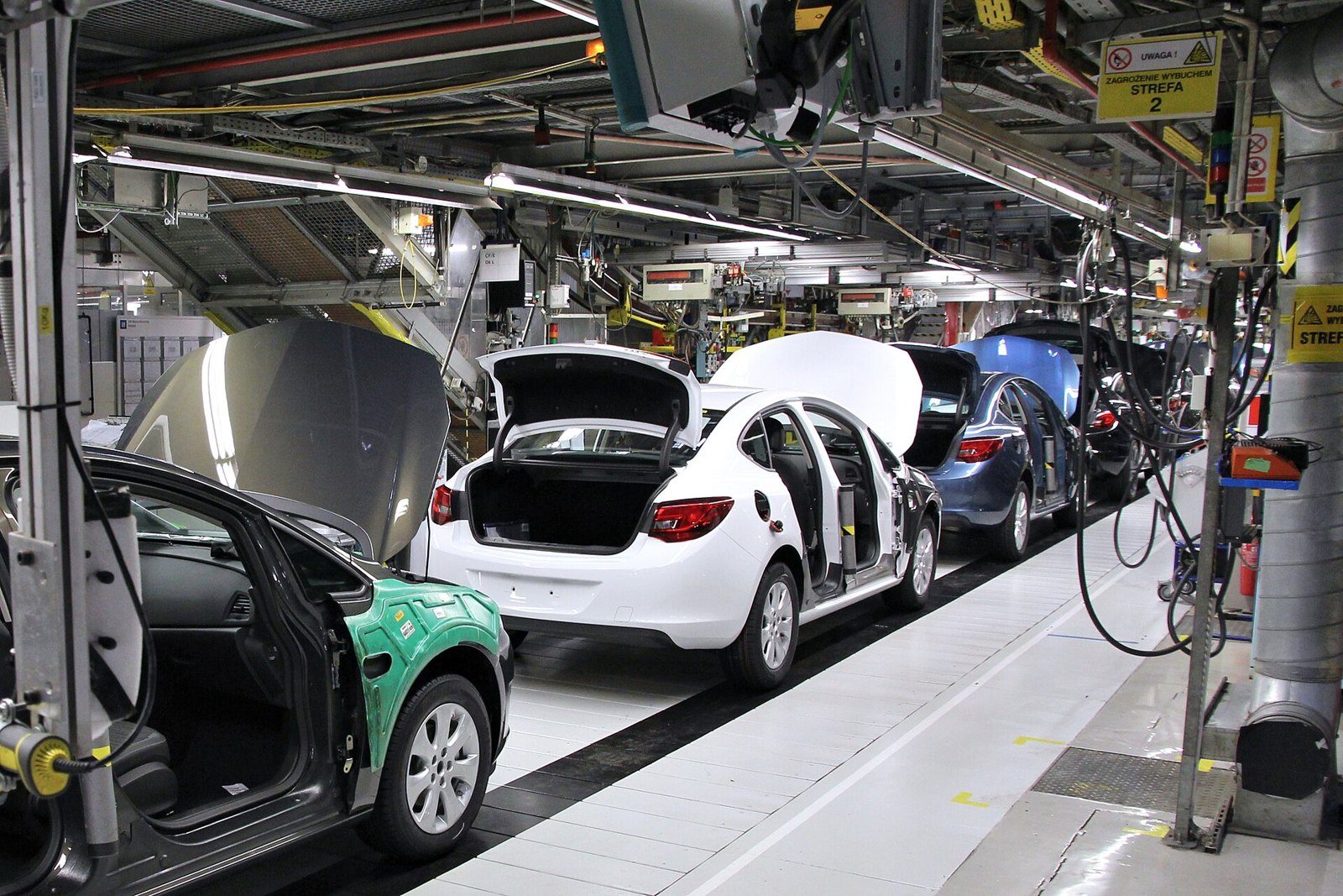 Línea de montaje de automóviles con carrocerías blancas, azules y verdes avanzando bajo estructuras de techo industrial